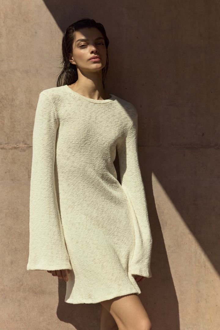Model wearing Bell Sleeve Mini Dress in crochet cotton knit with flared sleeves and a leg-lengthening mini silhouette in a breathable, lightweight knit.