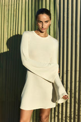 Model wearing a bell sleeve mini dress in natural tencel linen knit featuring flared sleeves and a leggy silhouette