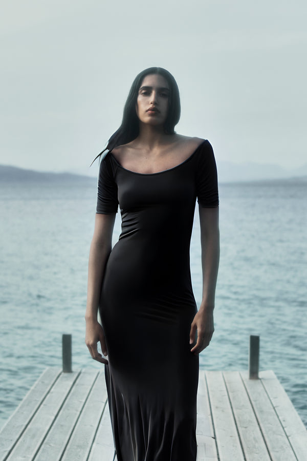Model wearing the Carolyn Off the Shoulder Midi Dress in Luxe Cupro Jersey, the graceful line of the neck continues to the shoulder and together with the elbow-length sleeve creating a moment of alluring and understated chic. 