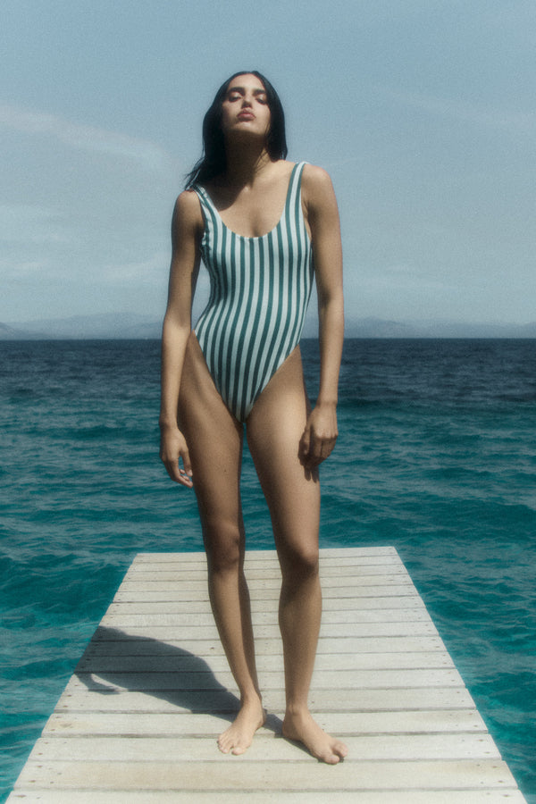 Model wearing the Hume One-Piece in Green Vertical Stripes featuring a high-cut leg and plunging back for a sleek, effortless look. 