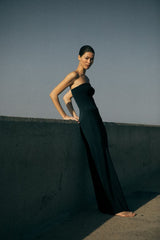Woman in a black strapless top and bias-cut maxi skirt against a plain background