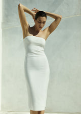 Woman wearing a white strapless dress standing against a white wall