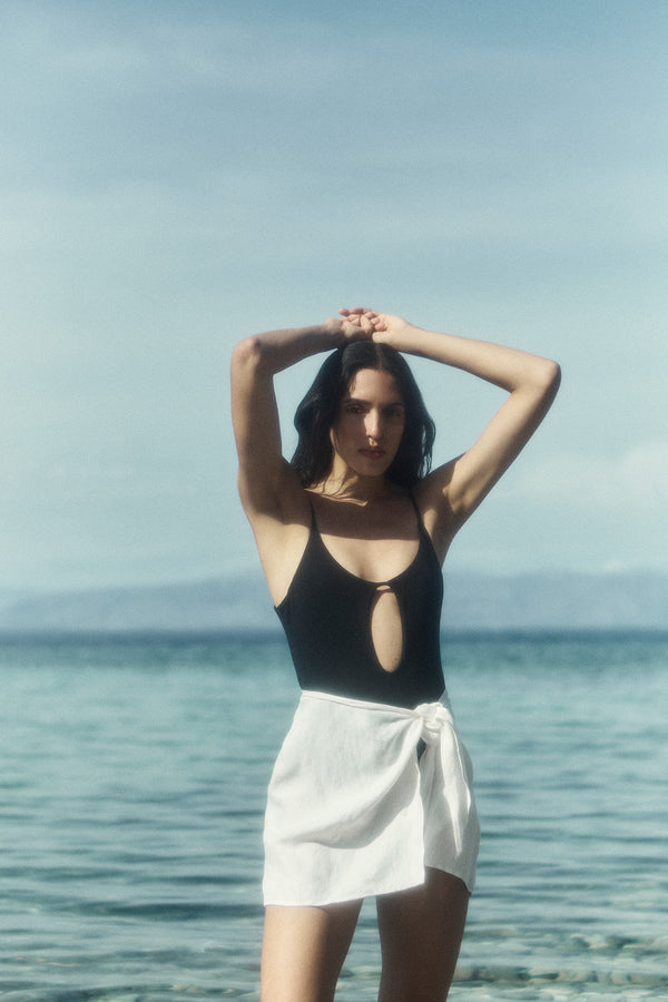Model wearing Wrap Mini Skirt Cover Up in Linen Cupro Blend White, with the comfort and simplicity of linen and a unique self-tie.